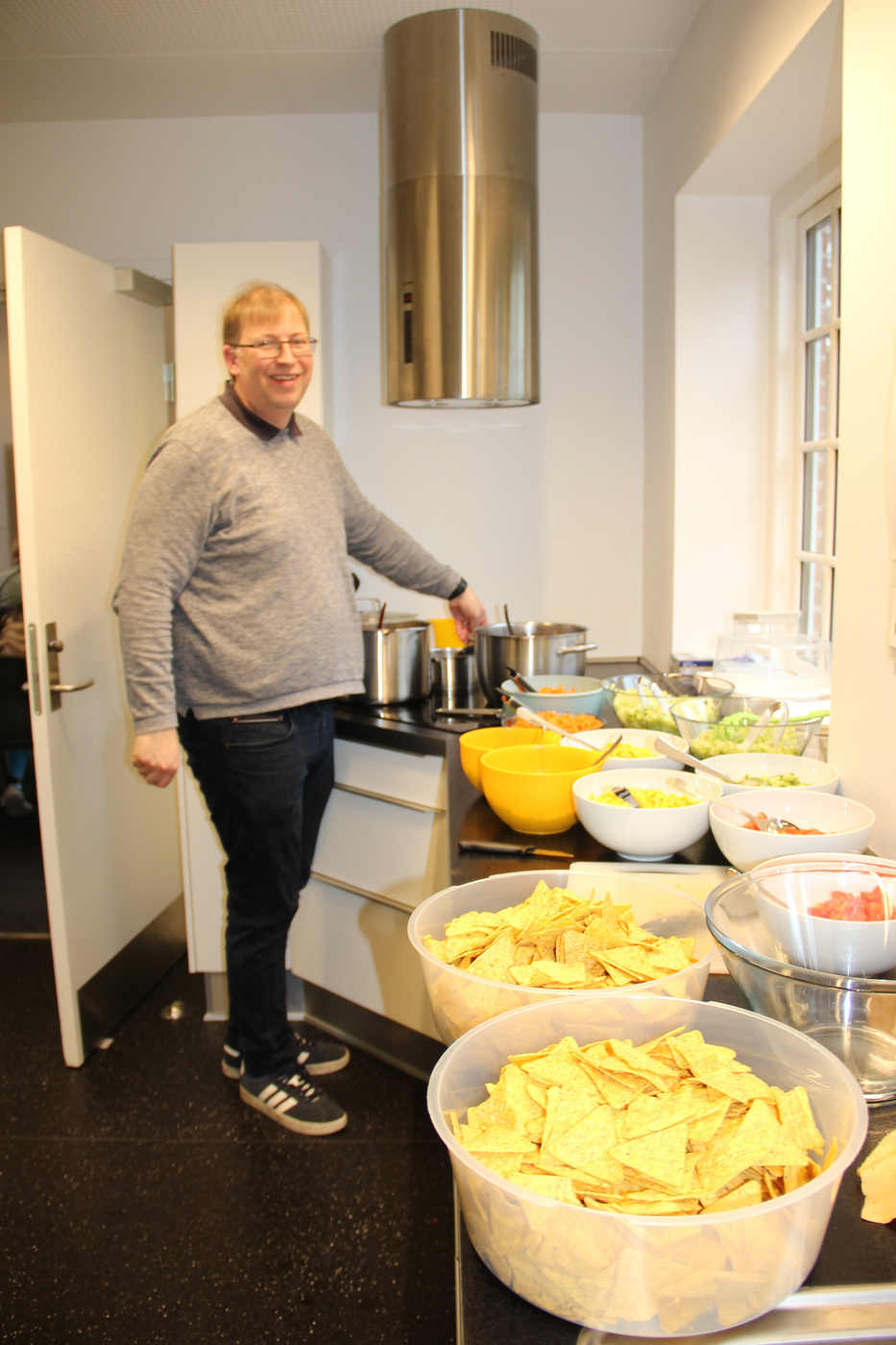 Mand står ved en buffet med skåle af chips og salater.