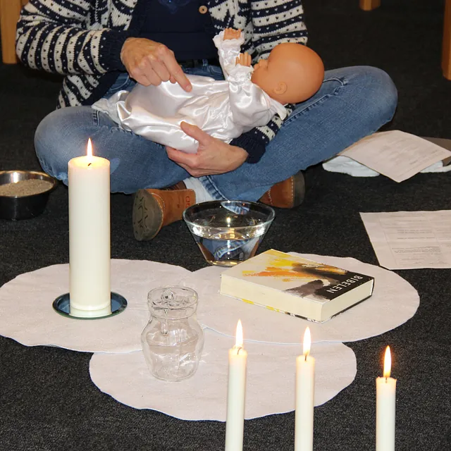Person holder en babydukke nær tændte lys, bibel og vand.