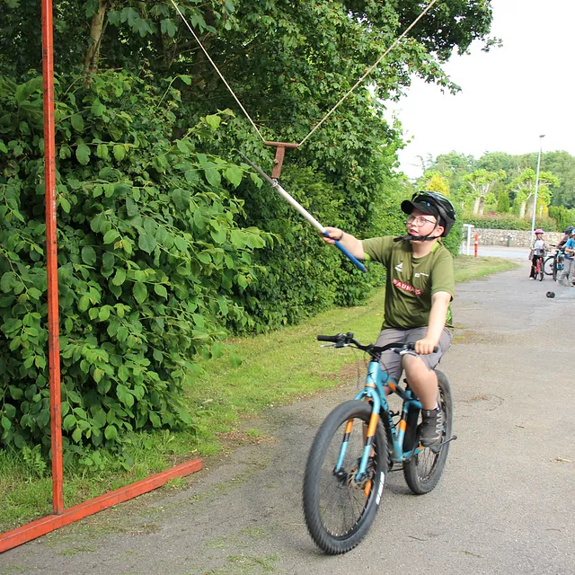 Dreng på cykel, med hjelm, rækker ud efter noget med en pind.