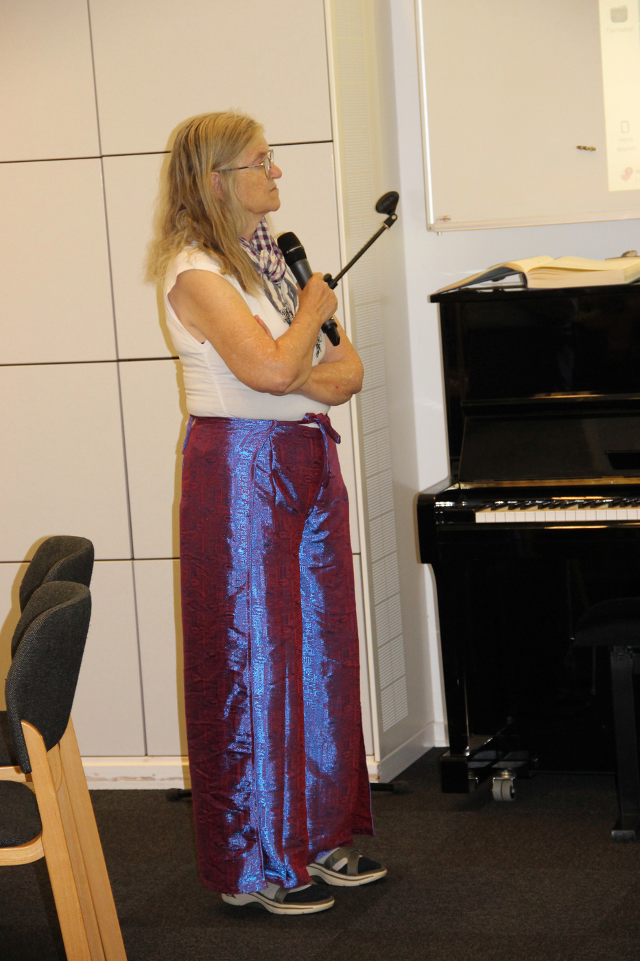 Kvinde i skinnende bukser holder en mikrofon ved siden af et klaver.