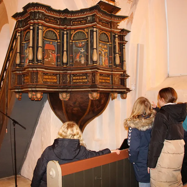 Børn kigger på en udsmykket, malet kirkeprædikestol.
