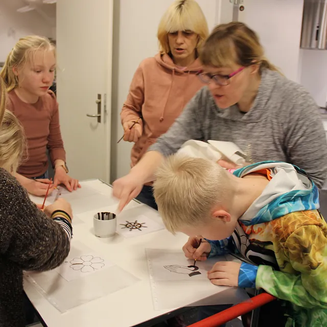 Voksne og børn pynter småkager ved et bord, en voksen vejleder.