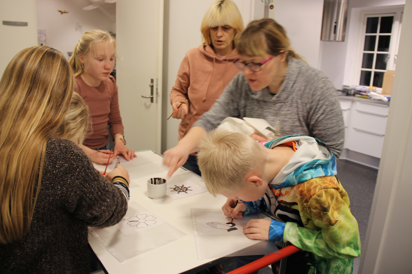 Voksne og børn pynter småkager ved et bord, en voksen vejleder.