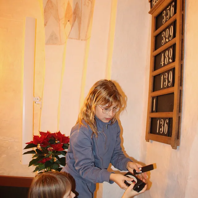 Pige smiler, rører ved en salmetavle i en kirke.