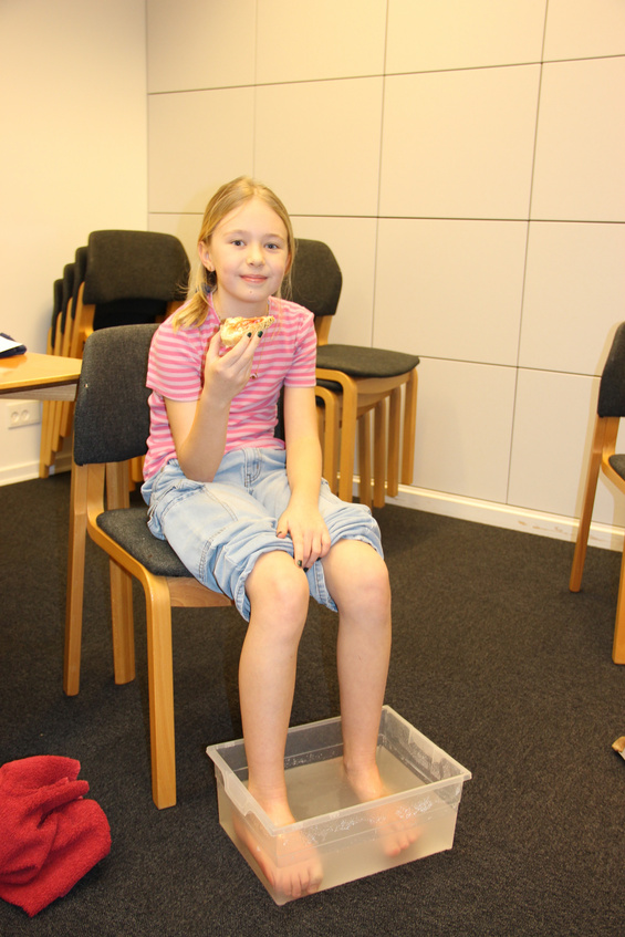 Pige smiler, fødderne i vand, holder et stykke bagværk i et kirkerum.