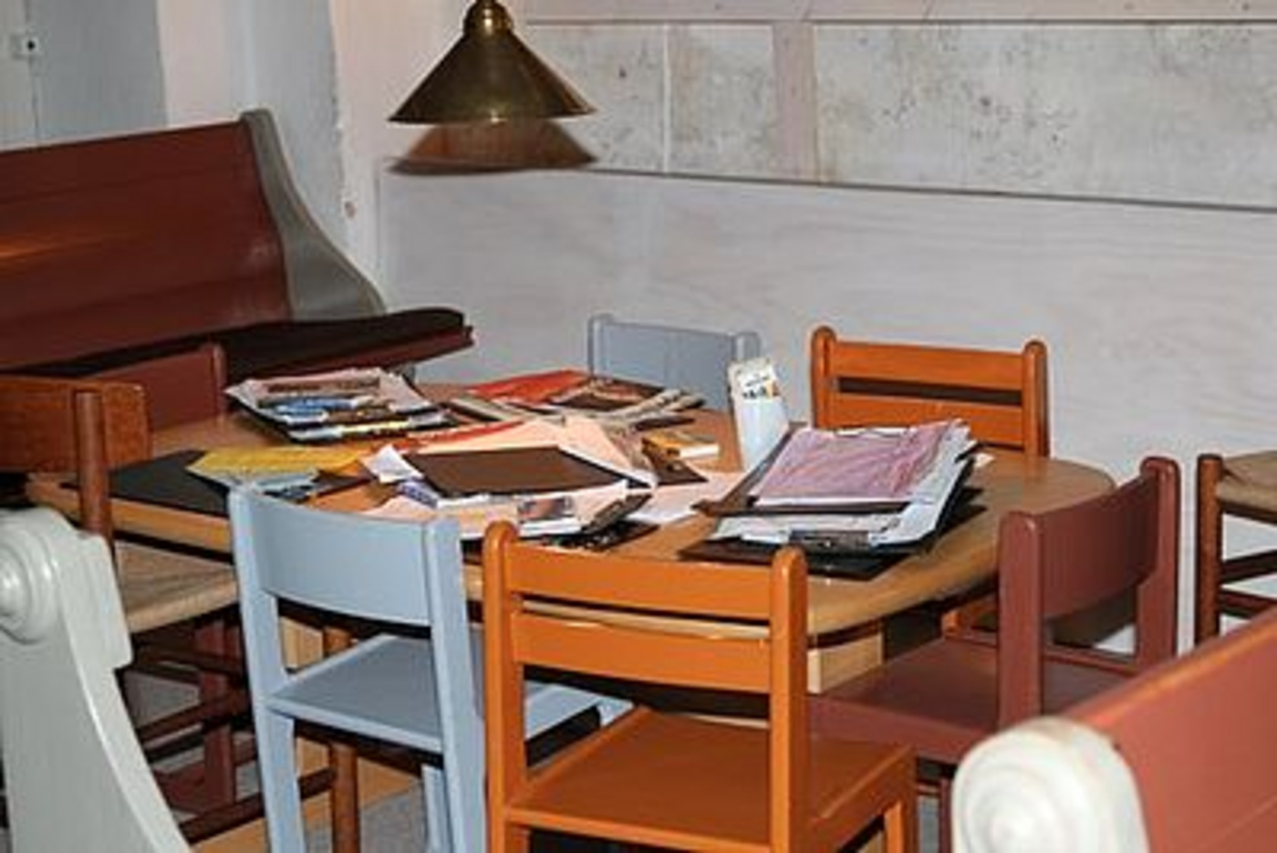 Rundt bord fyldt med papirer og bøger, omgivet af stole.