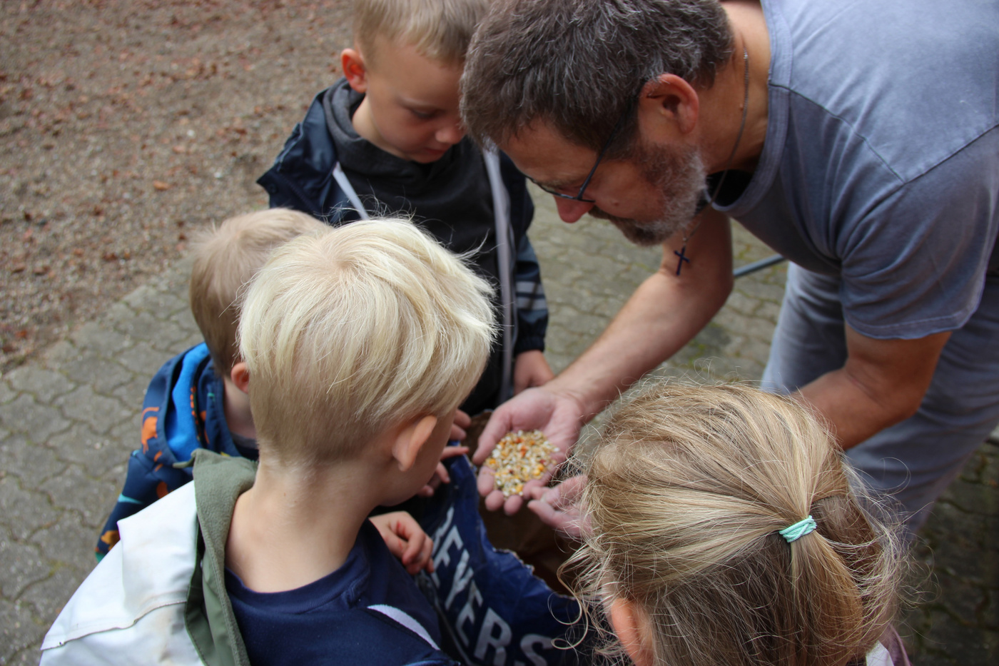 Mand med korshalskæde viser majskorn til tre børn.