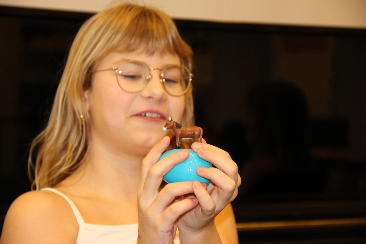 Pige med briller smiler, holder en lille legetøjsæsel på et blåt æg.