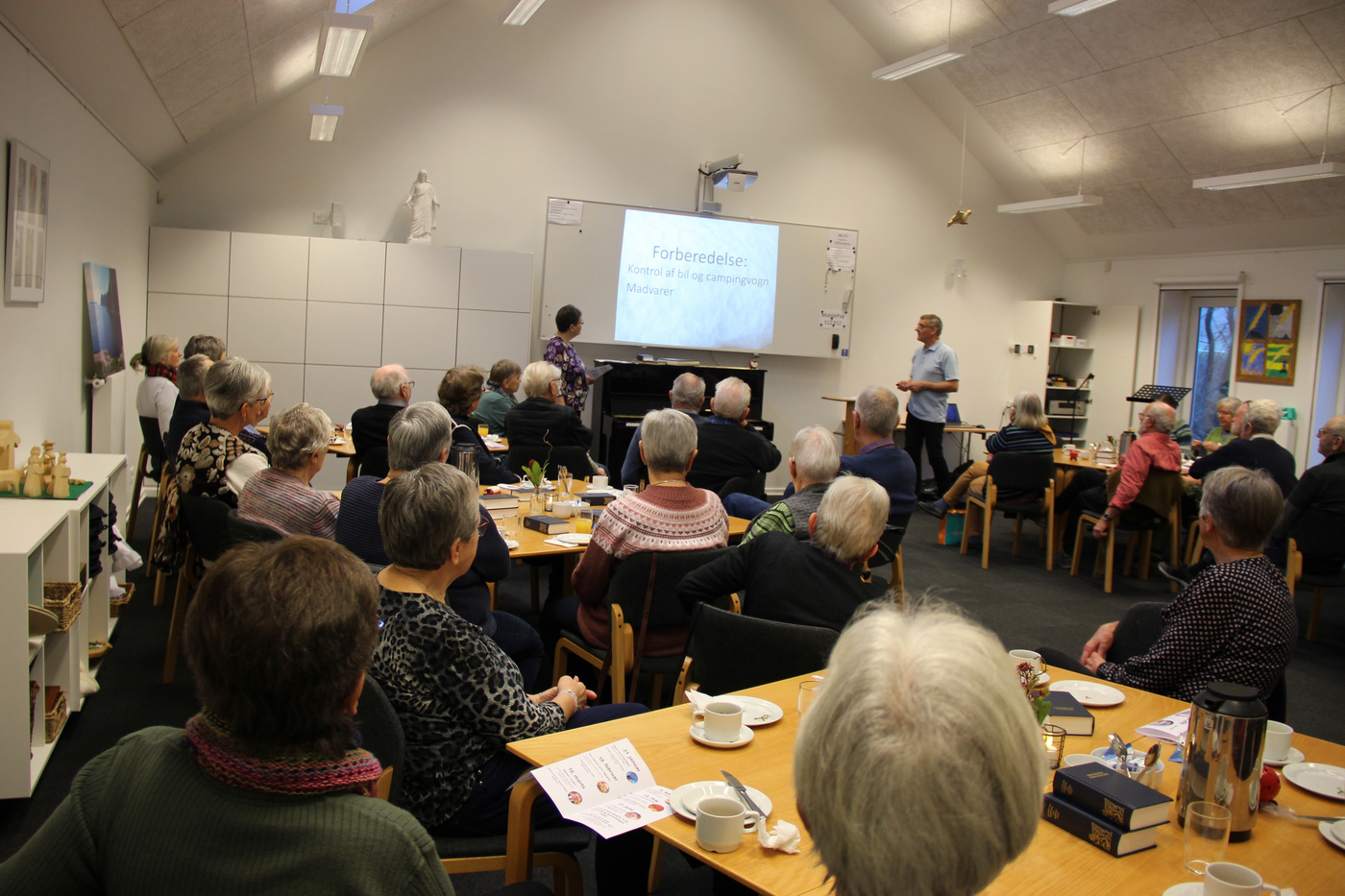 Stor gruppe voksne deltager i en præsentation i en kirkesal.