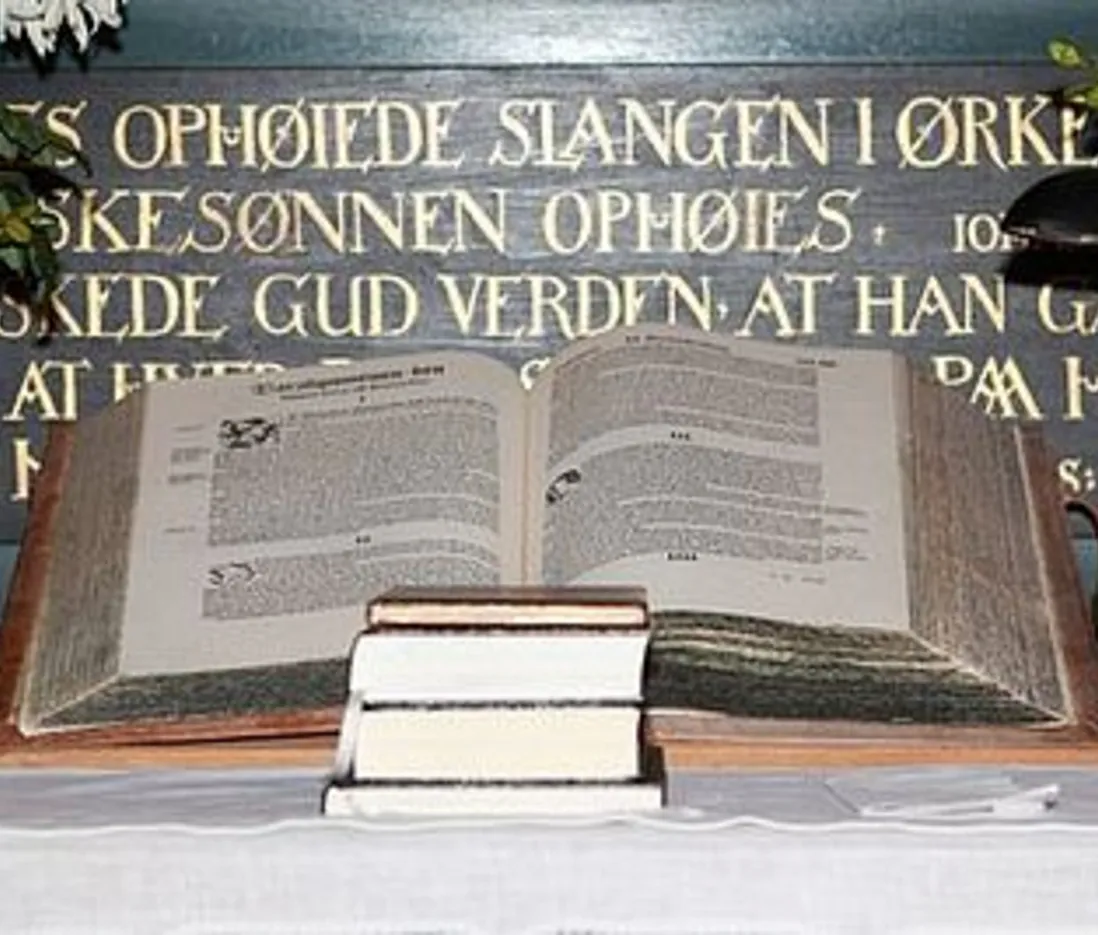 Åben bibel på stativ med salmebøger under, foran altertekst.