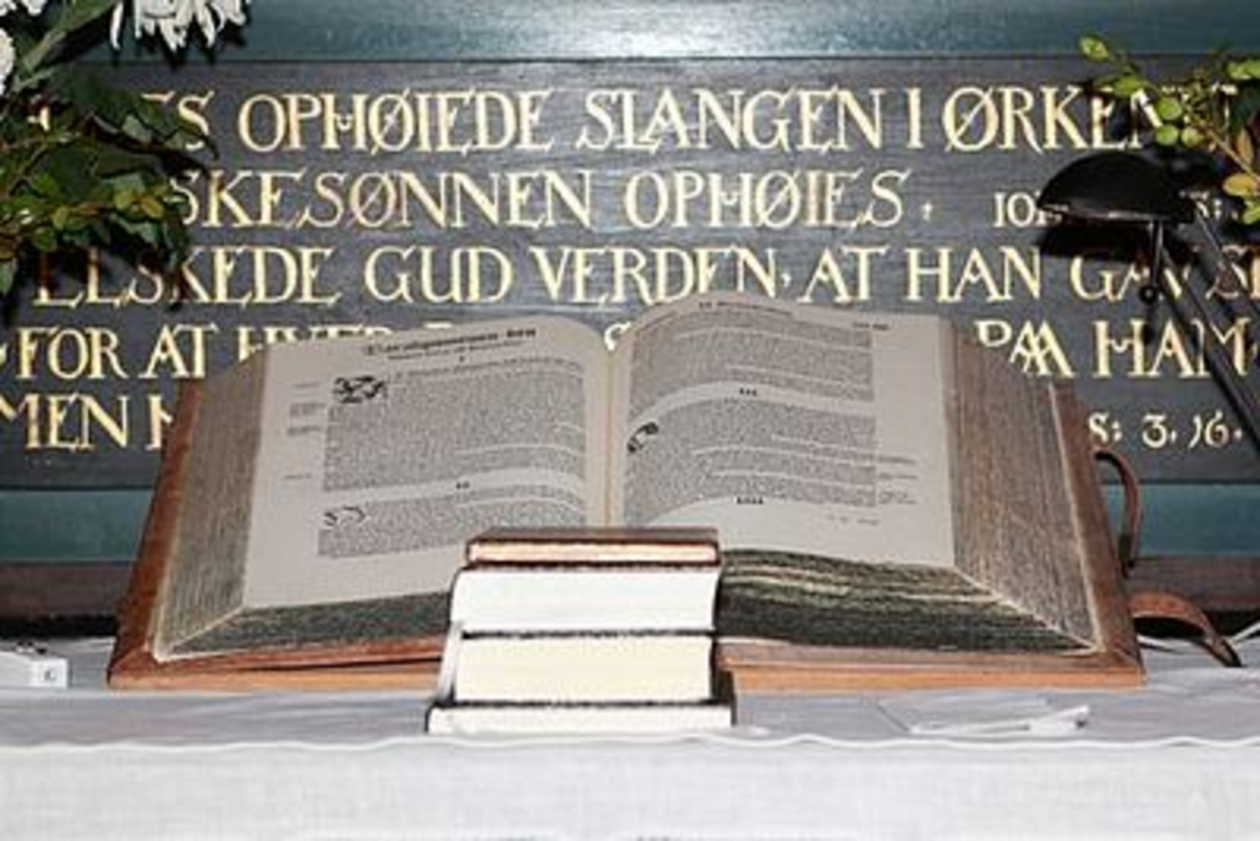 Åben bibel på stativ med salmebøger under, foran altertekst.