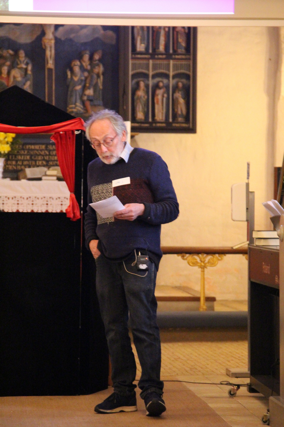 Mand med briller læser papirer, står nær alter i kirken.