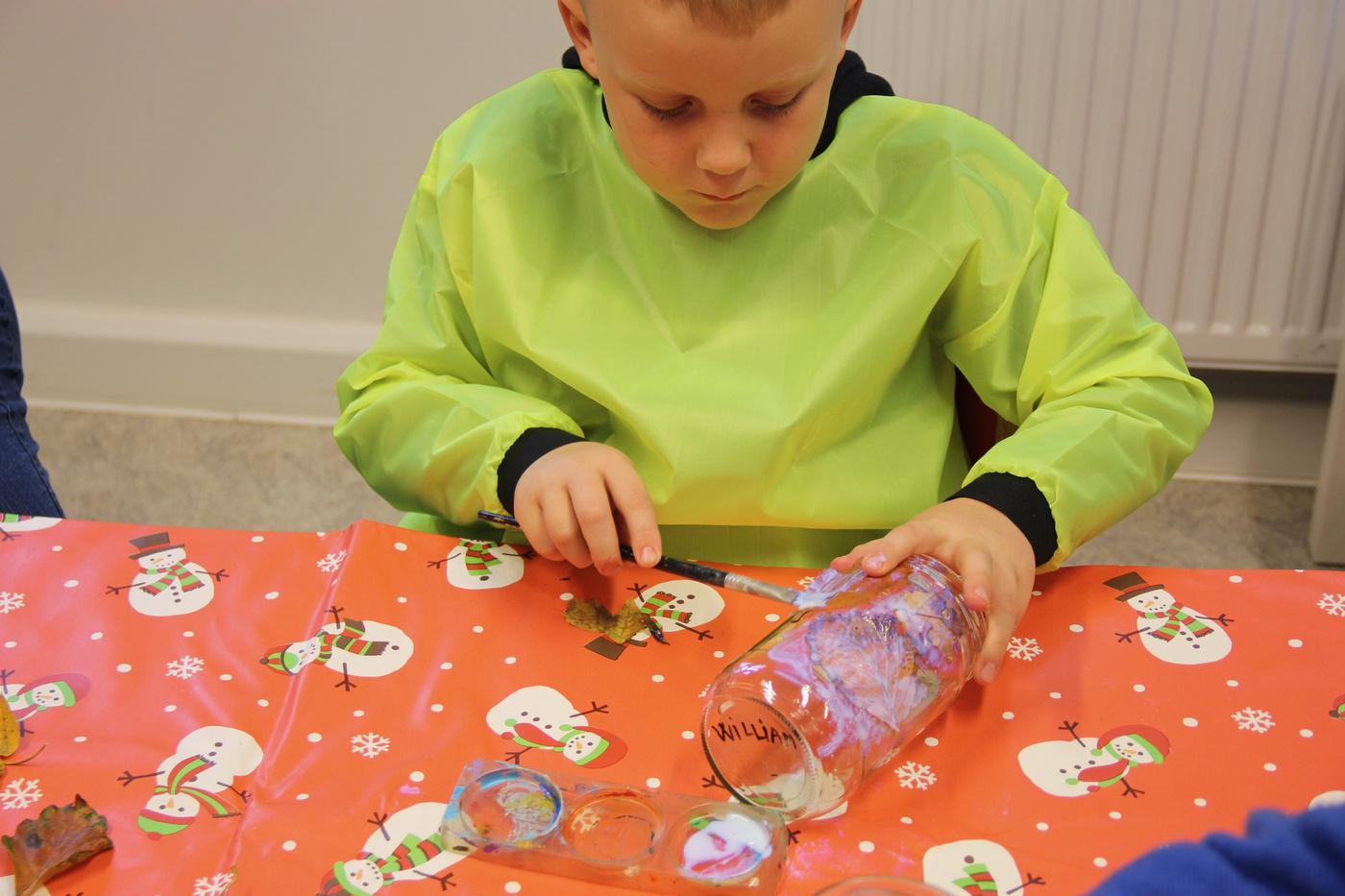 Dreng i kittel dekorerer en glaskrukke med maling.