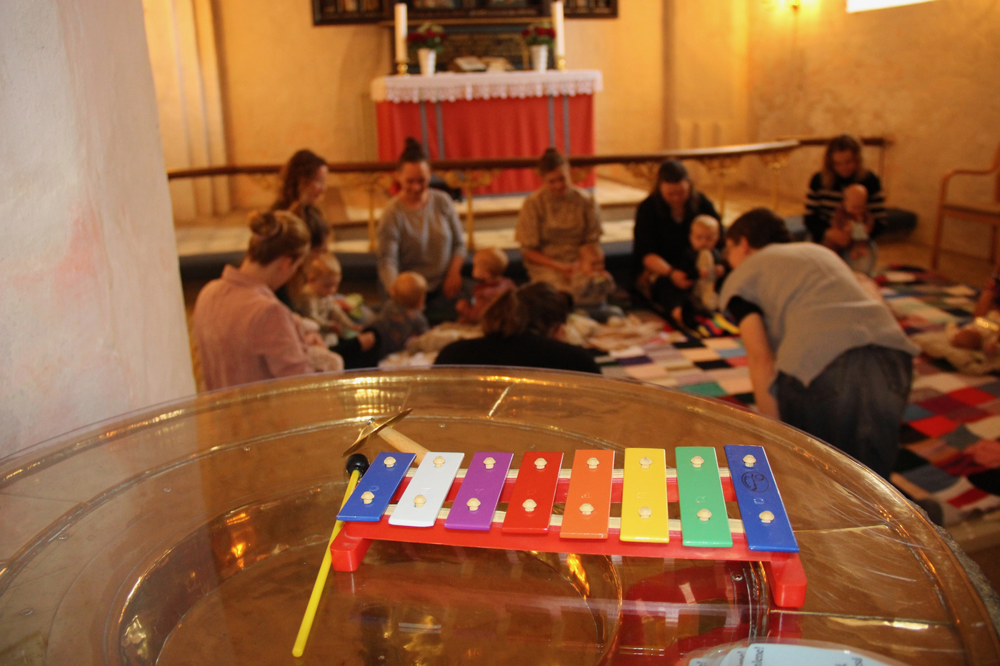 Xylofon i forgrunden, mødre og babyer leger i baggrunden.