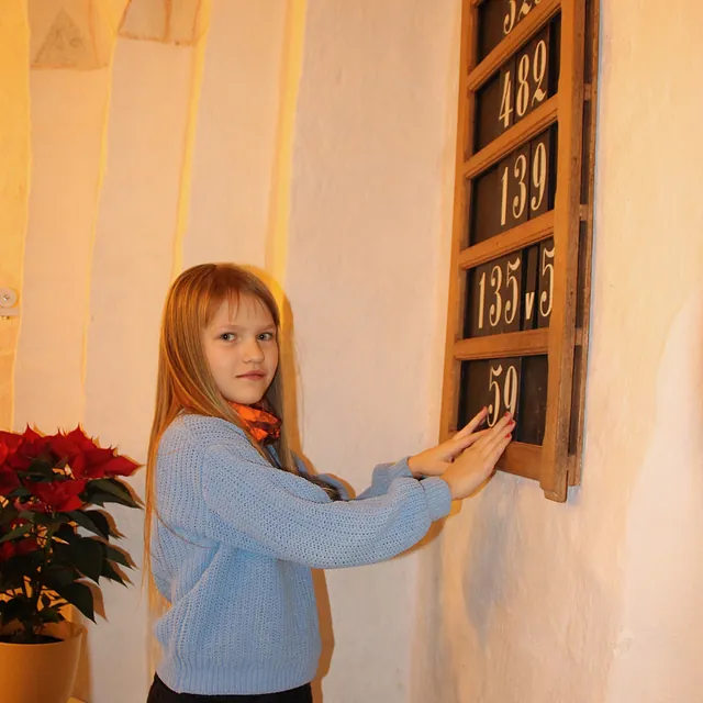 Pige smiler, rører ved en salmetavle i en kirke.