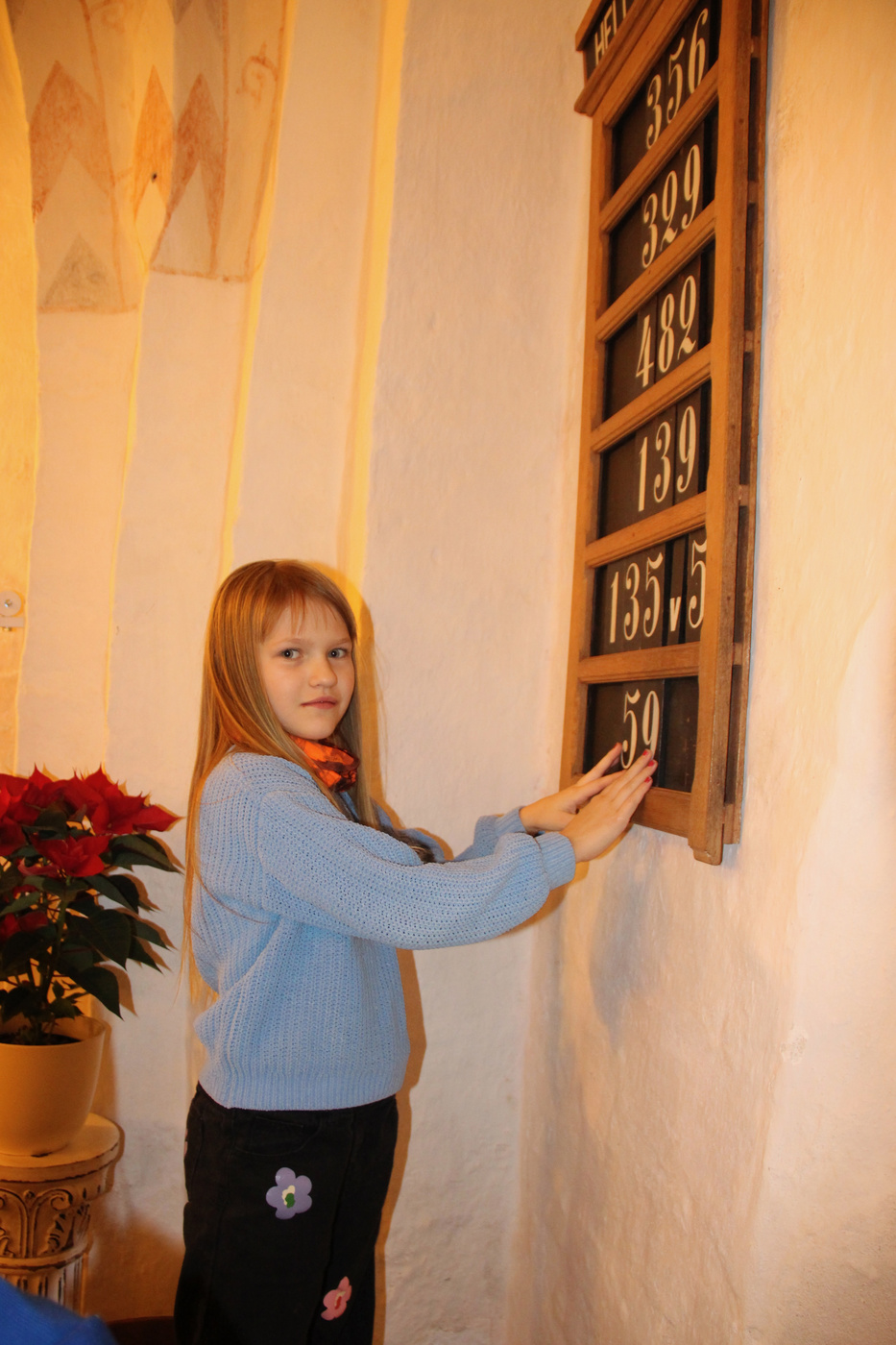 Pige smiler, rører ved en salmetavle i en kirke.