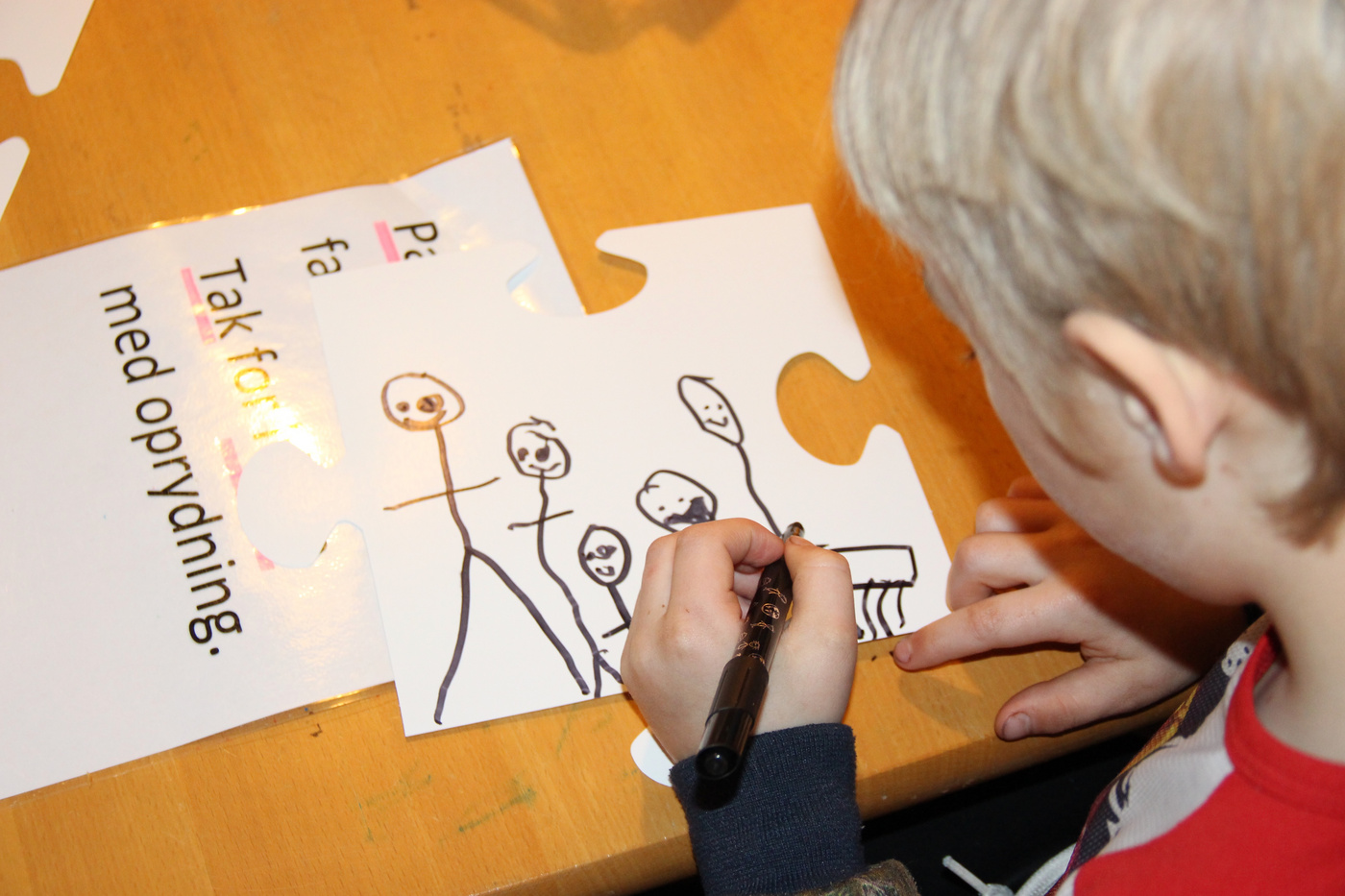  Børnetegninger samlet på store puslespilsbrikker på gulvet.