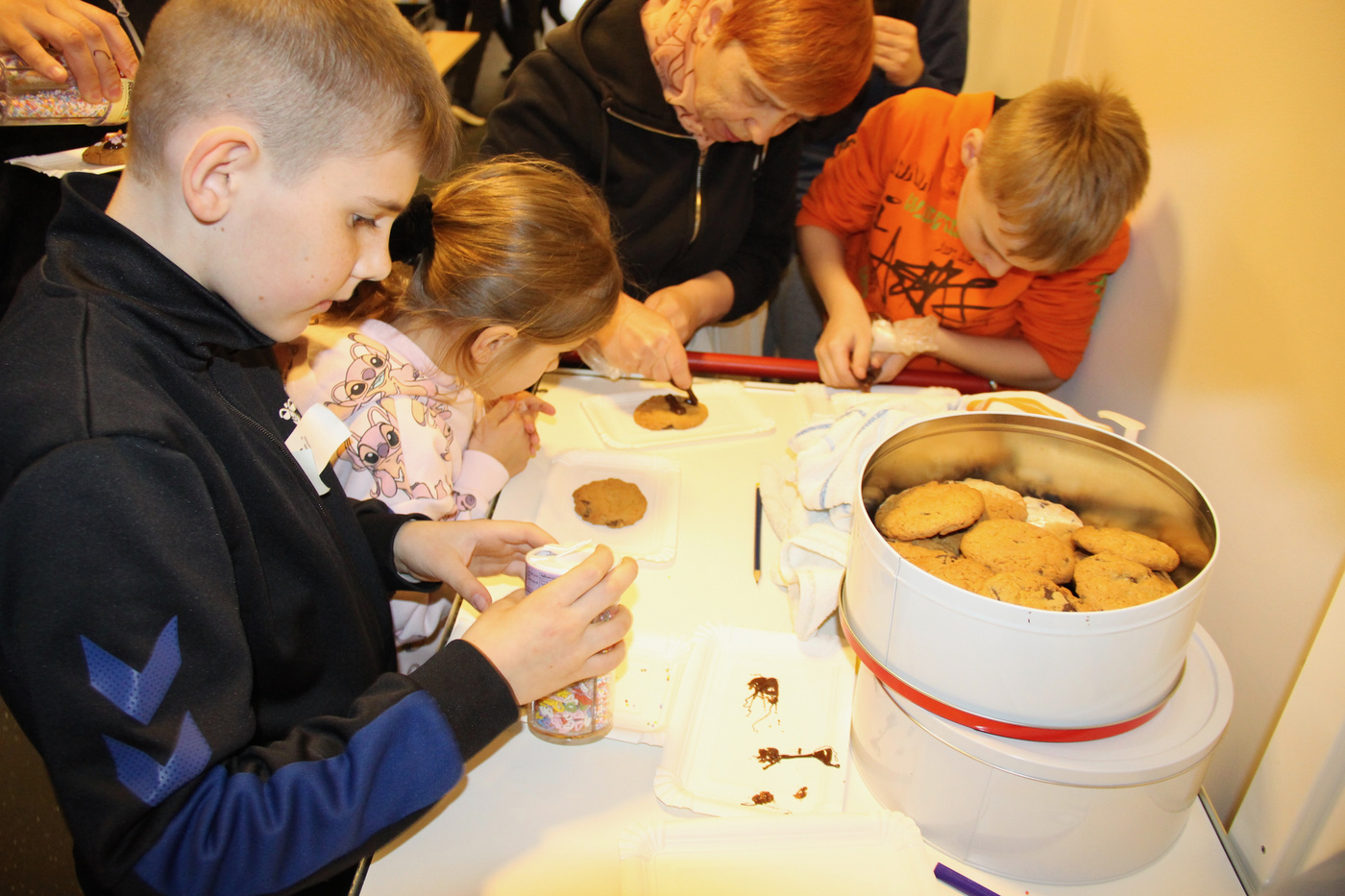 Børn og voksen pynter småkager med krymmel og glasur.