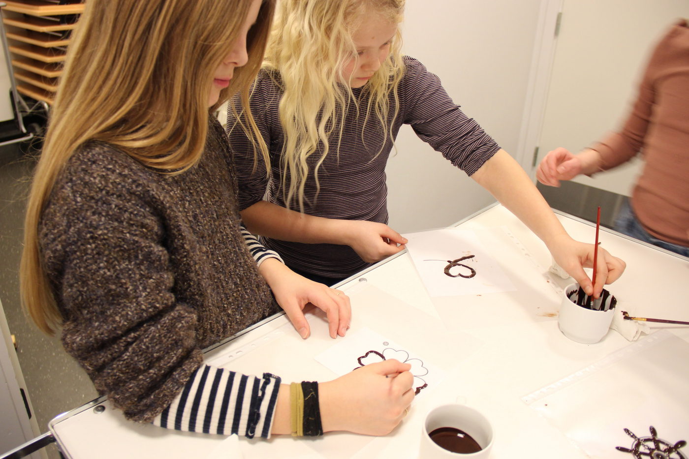 To piger pynter småkager med chokolade ved hjælp af pensler.