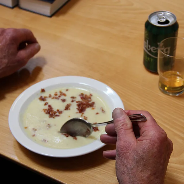Nærbillede af hænder, der spiser suppe med bacon, øldåse i nærheden.