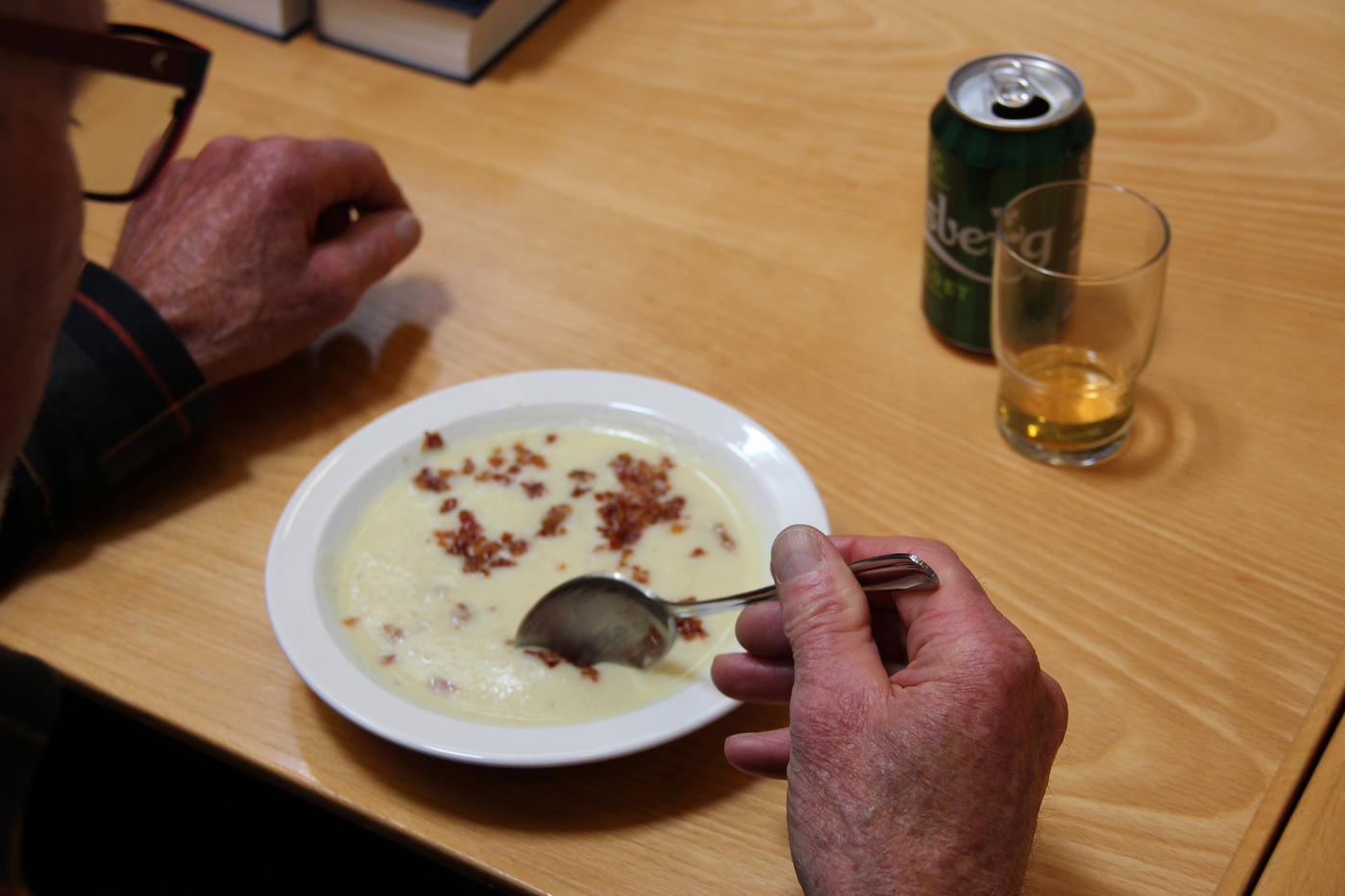 Nærbillede af hænder, der spiser suppe med bacon, øldåse i nærheden.