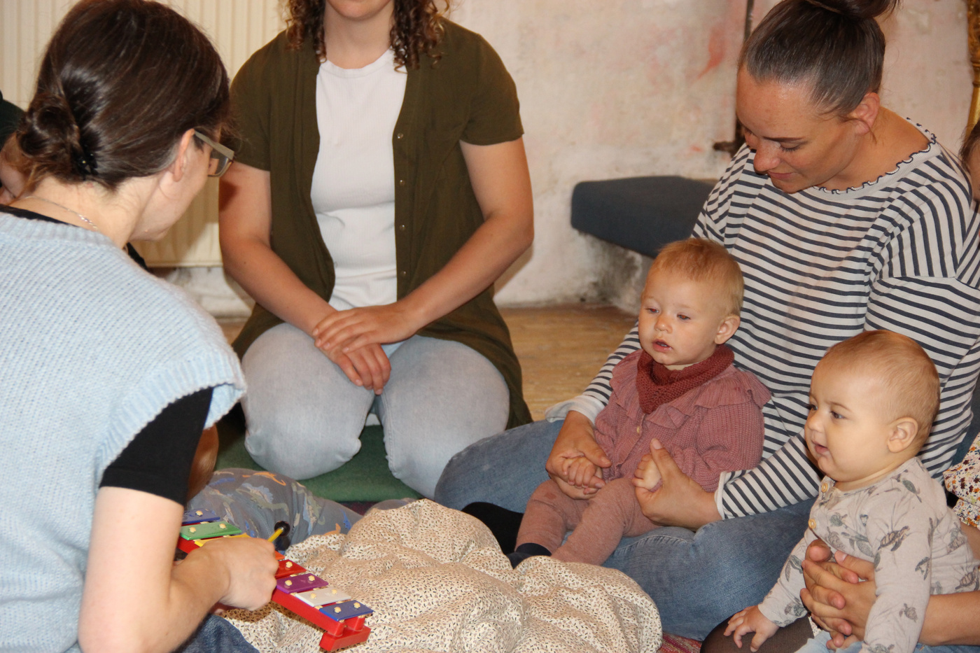 Mødre og babyer på gulvet, en leger med en legetøjsxylofon.