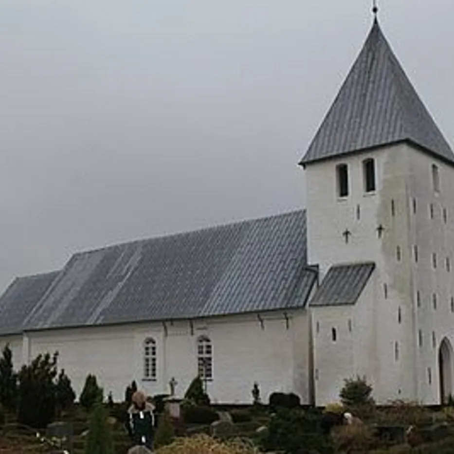 Hvid kirke med gråt tag og spir, omgivet af gravsten.