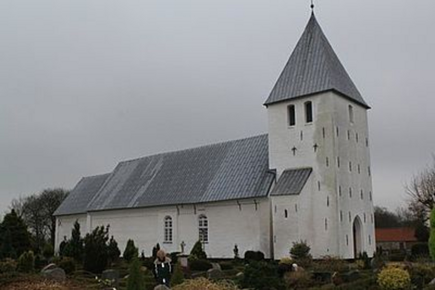 Hvid kirke med gråt tag og spir, omgivet af gravsten.