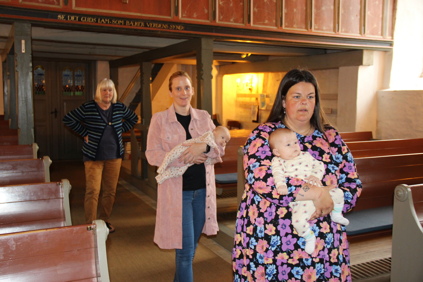 To kvinder holder babyer, en anden kvinde står i kirkens midtergang.