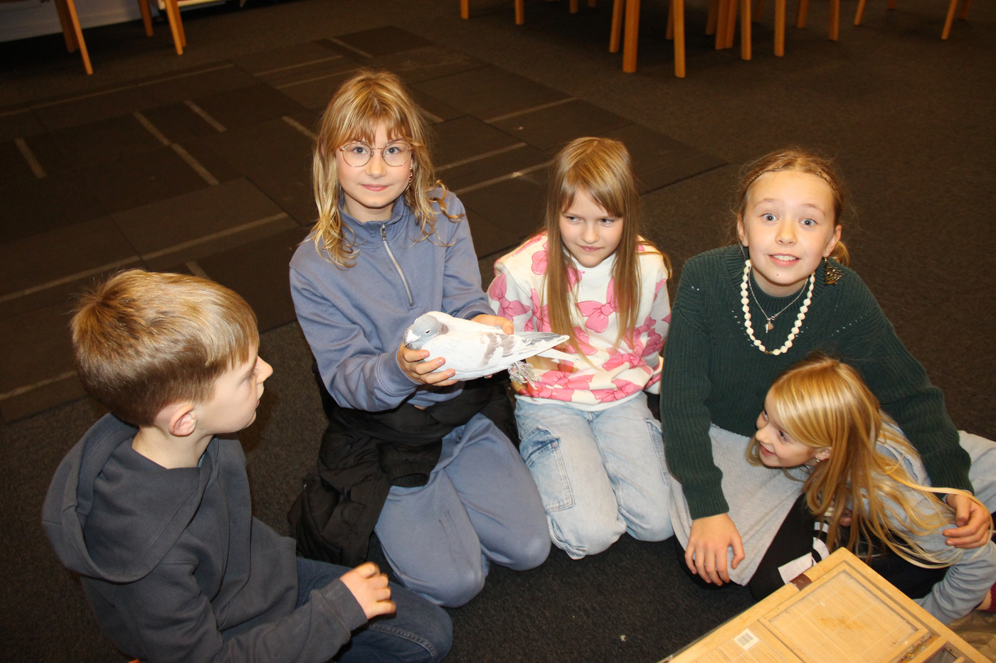 Fem børn sidder på gulvet, et holder en hvid due.