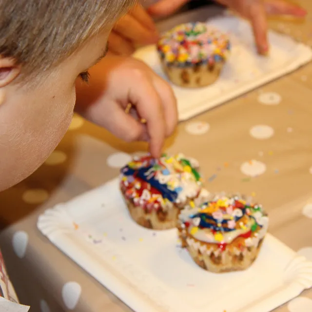 Nærbillede af et barn, der pynter cupcakes med farverigt krymmel.
