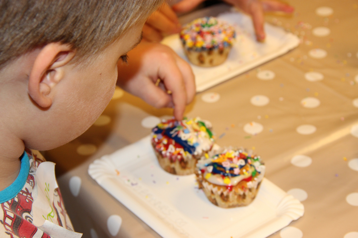 Nærbillede af et barn, der pynter cupcakes med farverigt krymmel.