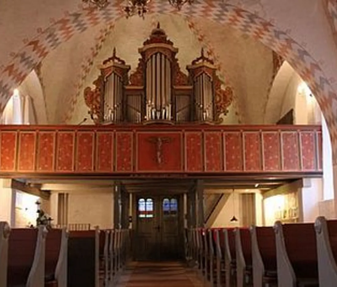 Kirkeinteriør med træbænke mod et stort pibeorgel.