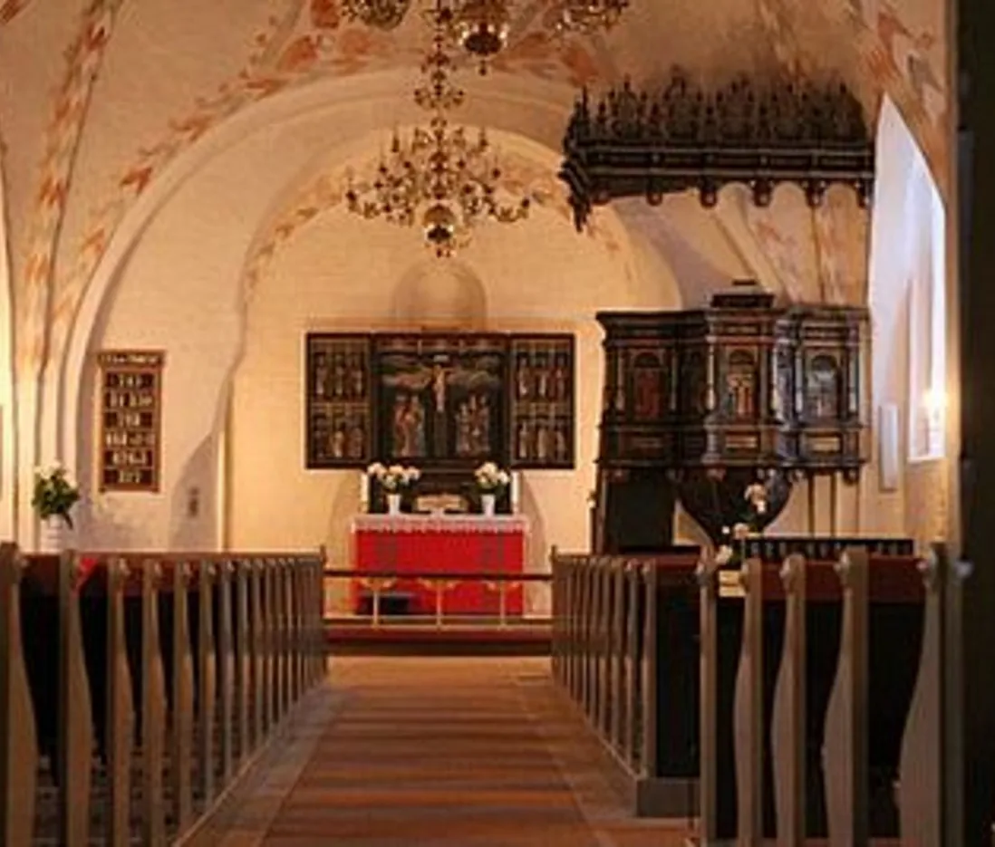 Kirkeinteriør med alter, prædikestol, kirkebænke og malede buer.