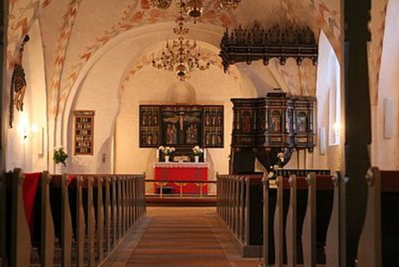 Kirkeinteriør med alter, prædikestol, kirkebænke og malede buer.