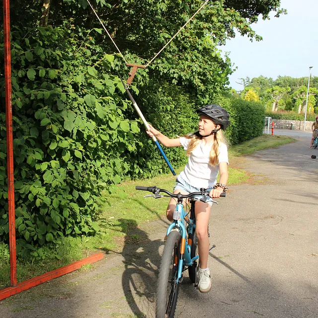 Pige på rød cykel, med hjelm, rækker ud efter et højt mål.