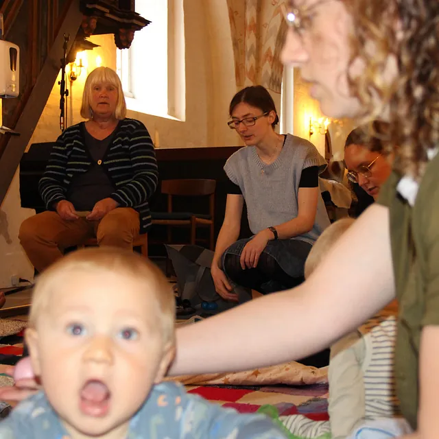 Baby kigger op, voksne og andre babyer i baggrunden i kirken.
