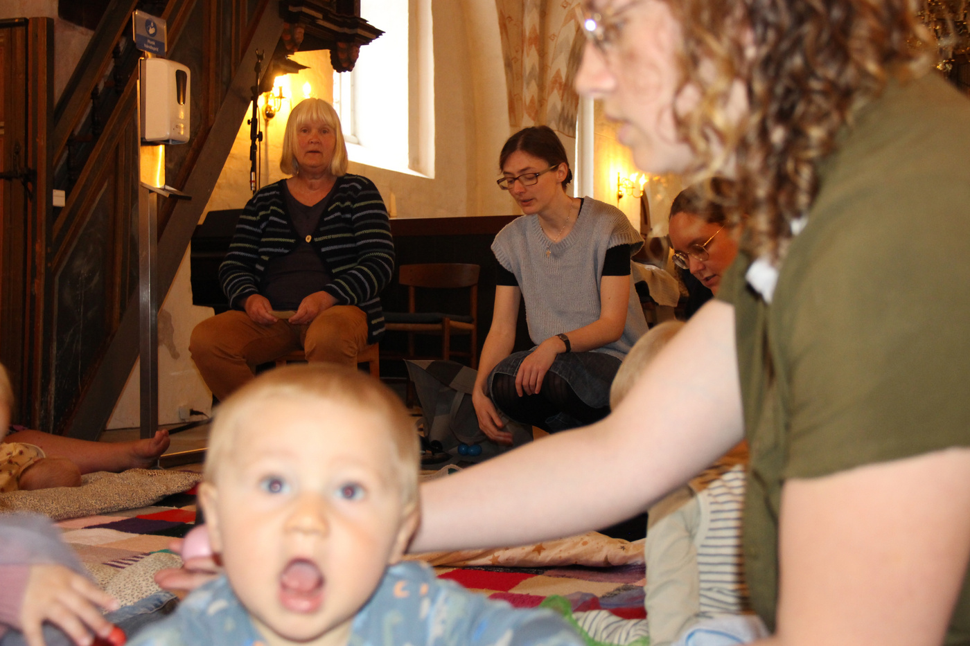 Baby kigger op, voksne og andre babyer i baggrunden i kirken.