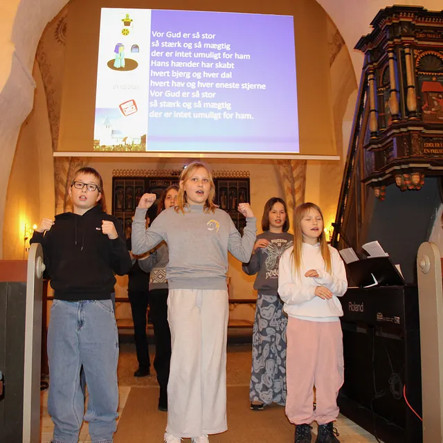 Børn synger entusiastisk i en kirke med projicerede tekster.
